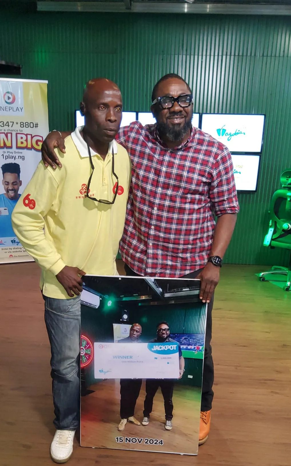 nyang and Chiboi smiling and holding a photo from Inyang’s previous ₦1 Million Oneplay jackpot win on Wazobia FM